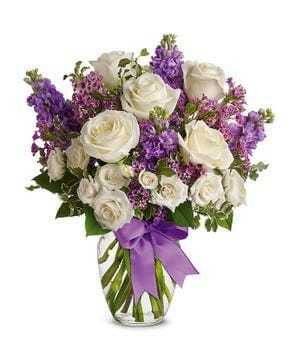 Enchanted Cottage bouquet featuring white full-size roses, white spray roses, lavender stock, and waxflower, elegantly tied with a lavender satin ribbon.