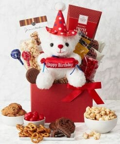 a red basket with a white and red teddy bear with chocolate and birthday gift basket treats.