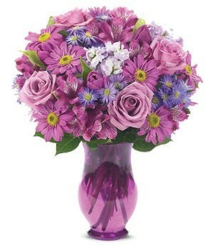 Springtime Lavender bouquet featuring lavender alstroemeria, daisies, roses, tulips, and waxflower arranged in a purple vase - Available for same-day flower delivery.