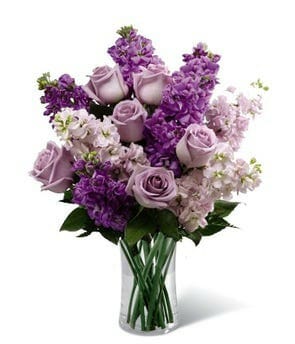 Spring Bursting Forth bouquet featuring lavender roses, lavender stock, pink stock, and lush greens in a contemporary cylinder vase - Available for same-day flower delivery.