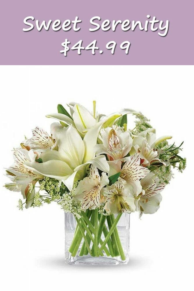 A beautiful short square clear vase with lilies and white flowers for a sympathy gift.