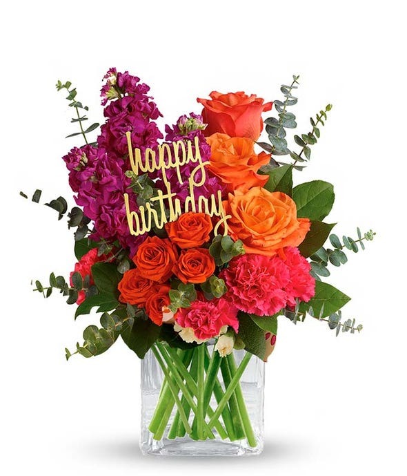 A full birthday bouquet of orange and red flowers with greenery and a happy birthday pin.