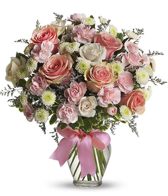 Pink and white roses with green poms arranged in a clear glass vase.