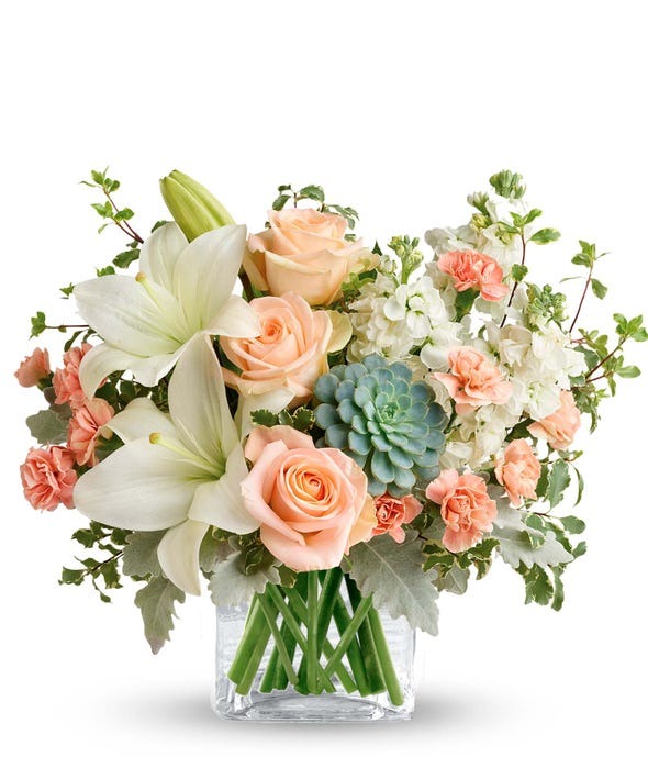 Peach colored roses and white flowers mixed with greenery in a clear glass vase.